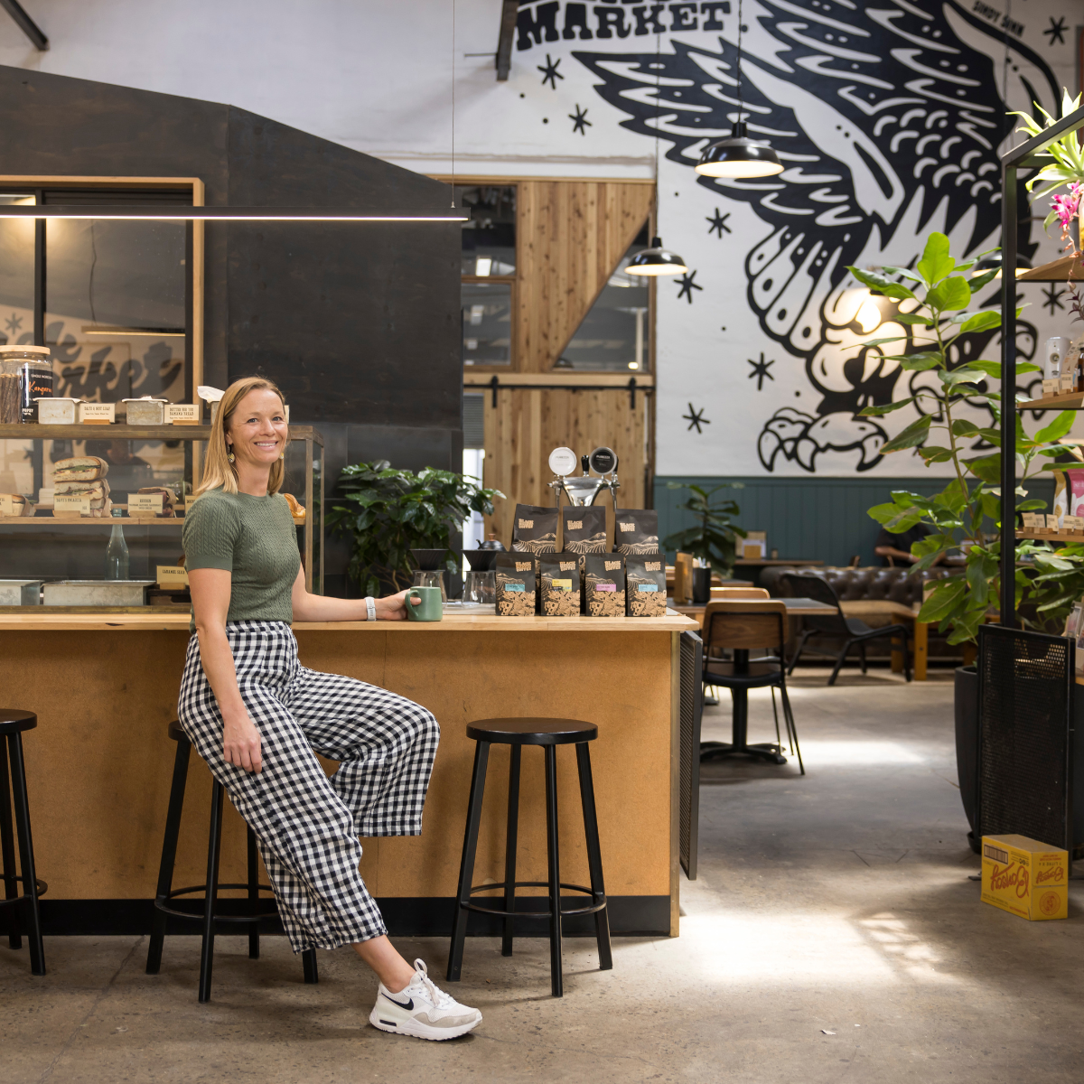 Jess sitting on a stool in a modern cafe with a decorative wall mural.