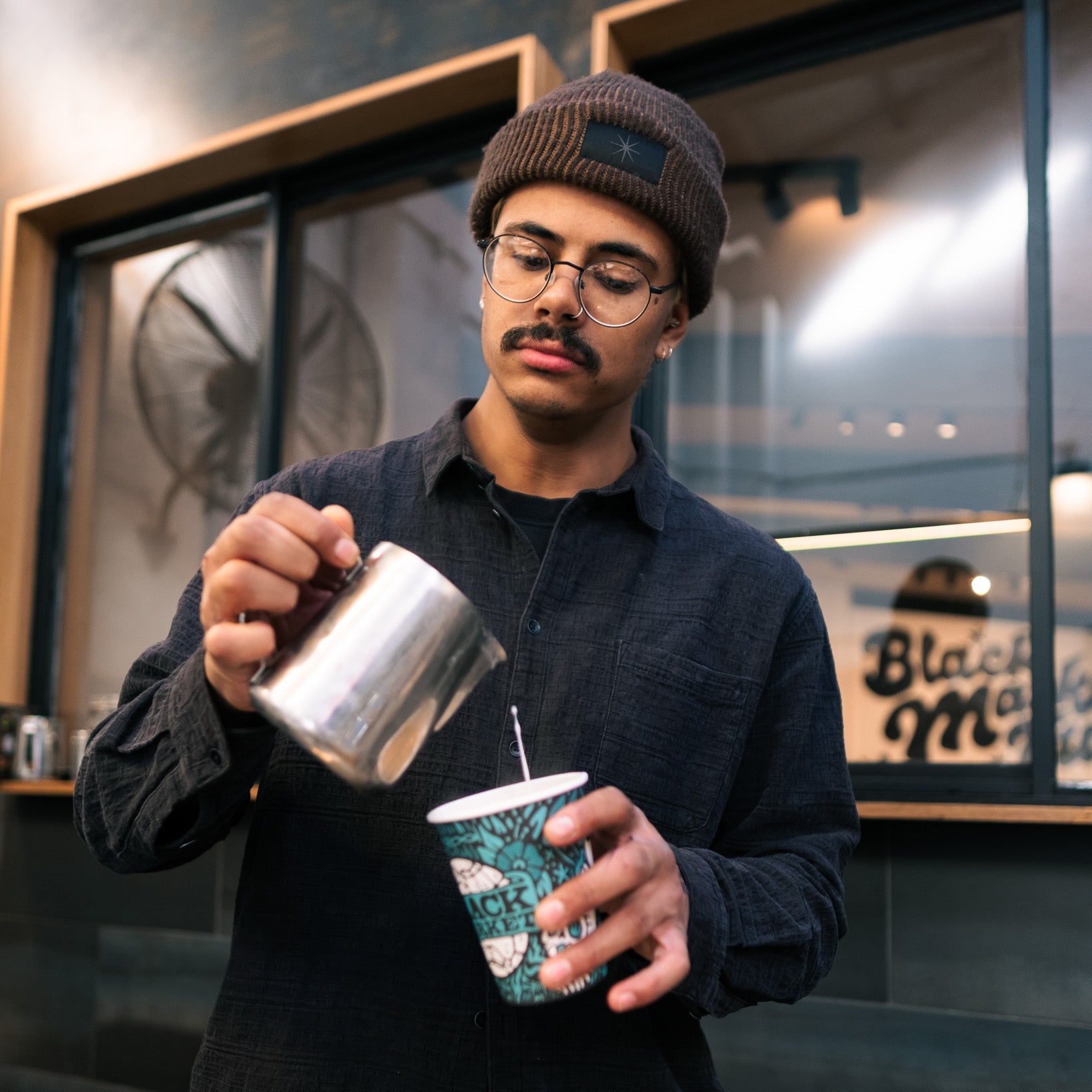 Barista pouring milk into a coffee cup in a coffee shop.
