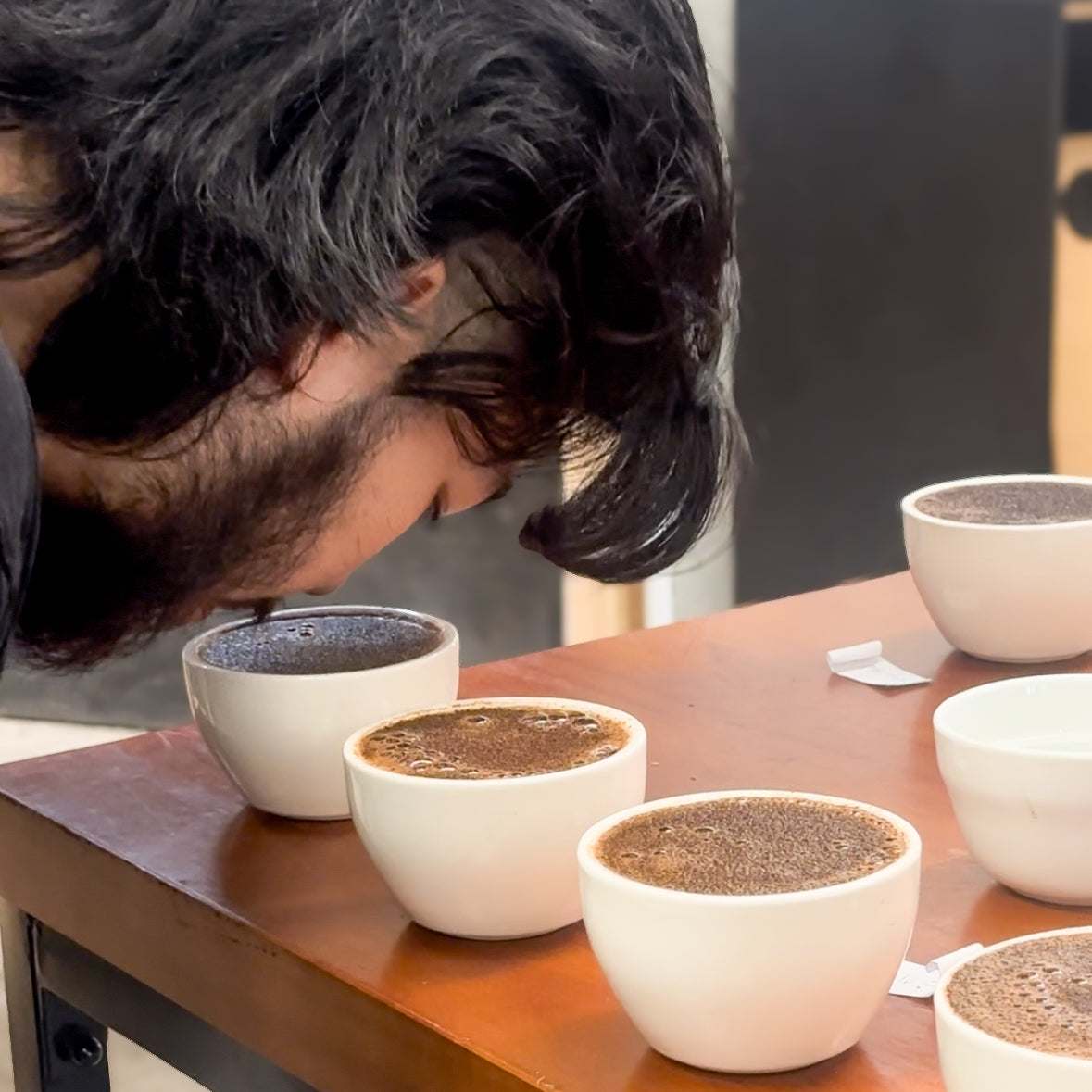 Person smelling coffee in small white cups on a wooden table